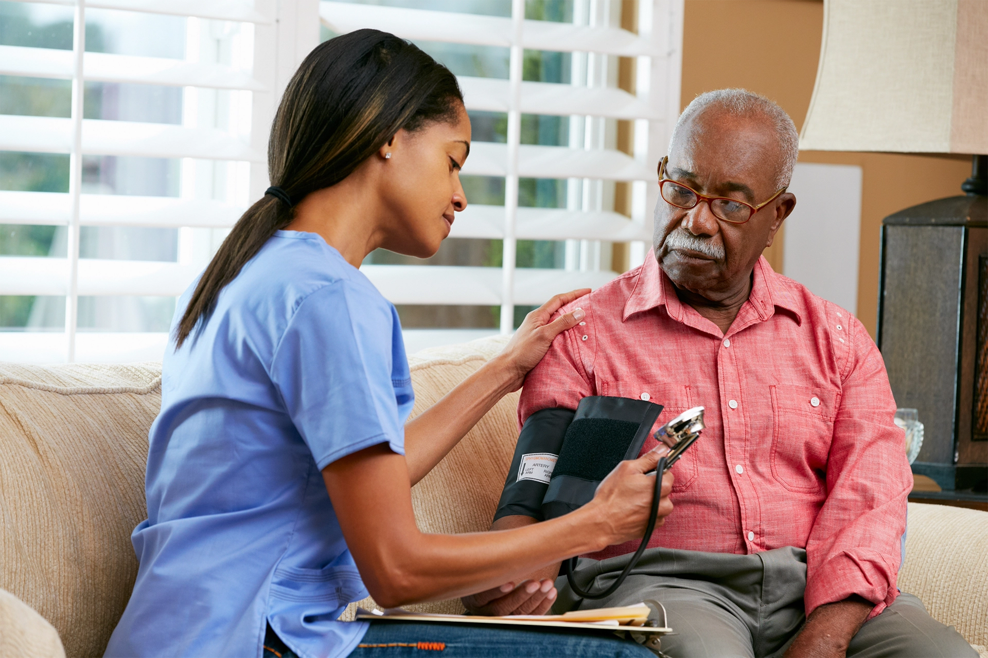 Home health nurse monitoring blood pressure for senior patient at home